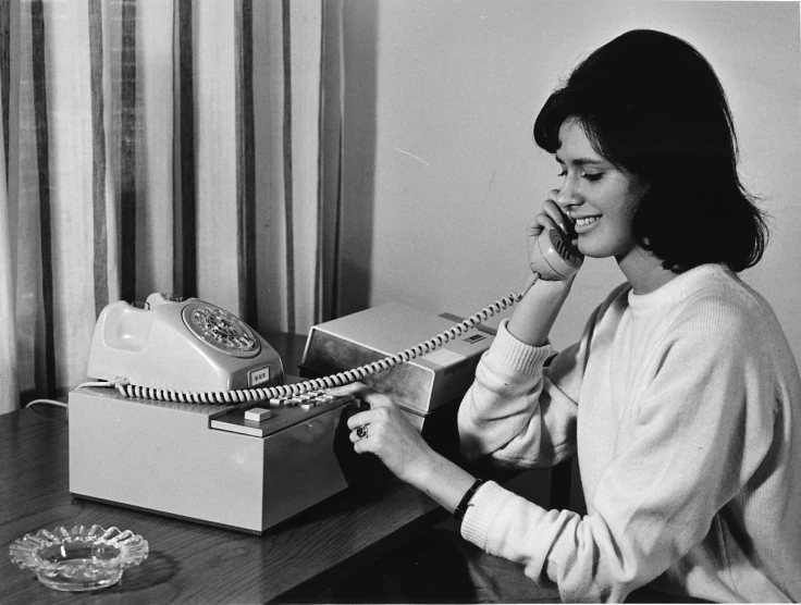 a woman sitting on a table while using an old phone