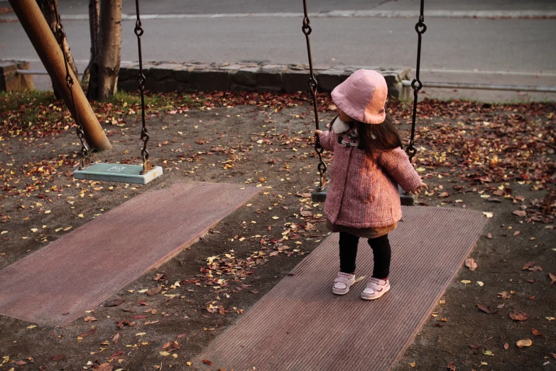 little girl with pink hat on a swing playing in fall leaves