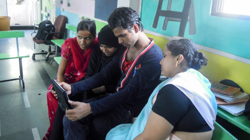 people sit on a bench looking at an electronic device