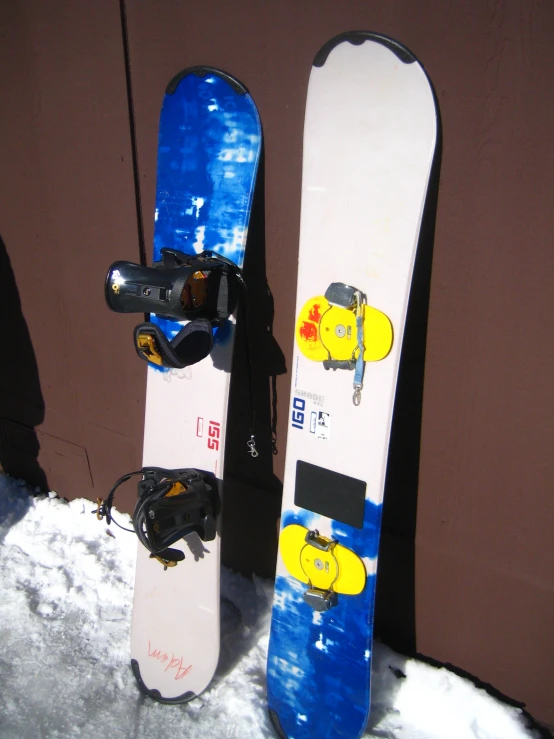 two snow boards leaning against a wall, with snow on the ground