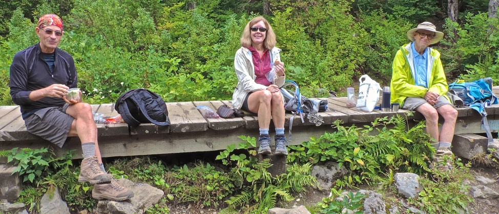 four people sitting on the side of a bridge eating and talking