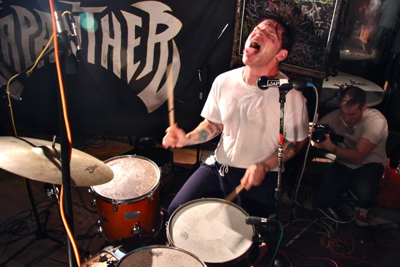 a man is singing while drumming in a band