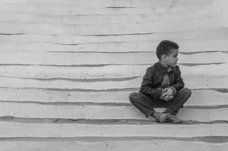 a small boy sits on some steps while holding his hands together