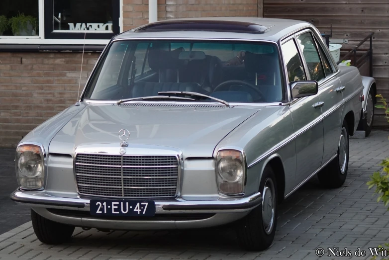 an old mercedes car sits parked in front of a brick building