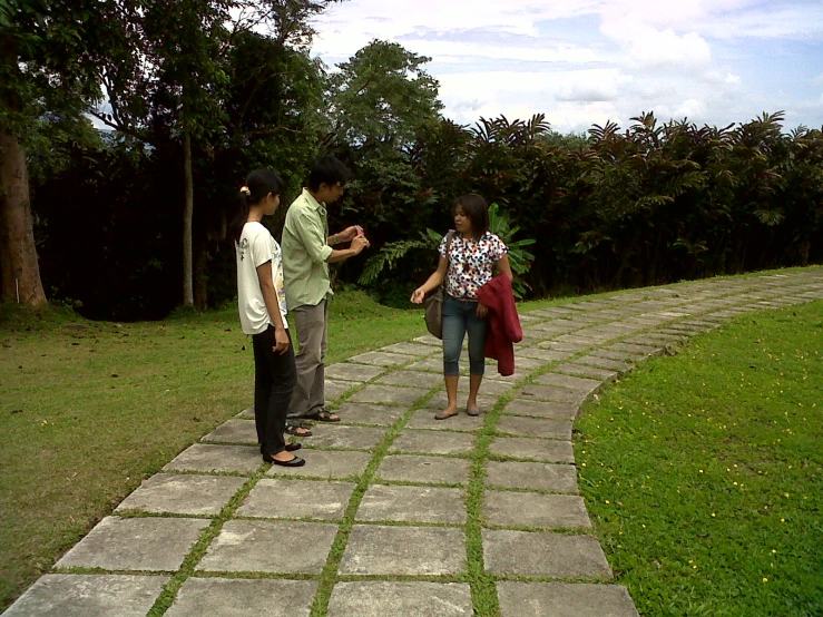 two men and a woman stand on a sidewalk near a grassy park