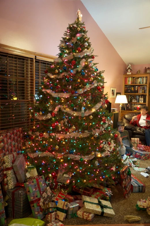 a living room with a christmas tree, presents and children