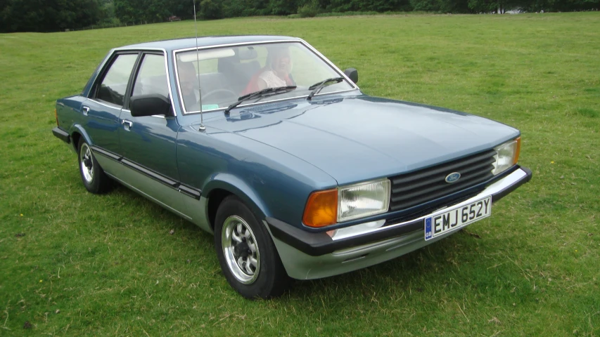 a blue car sitting in the grass in front of trees