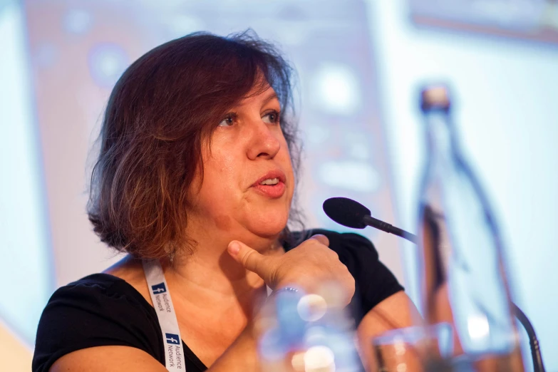 a lady talking into a microphone with a bottle in front