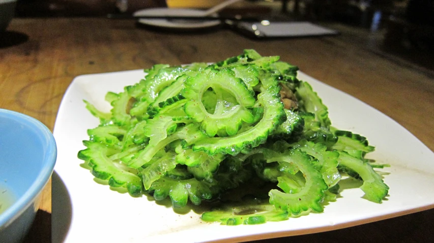 a square plate containing broccoli covered in green sauce