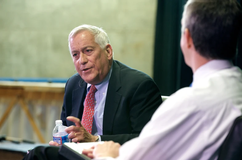 two men sitting at a table talking in front of a camera