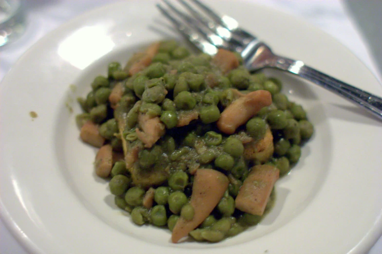 a plate with peas and carrots and some silver forks