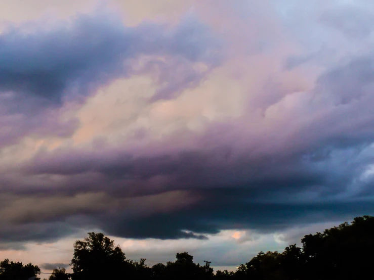 an image of dark clouds and trees during a sunset