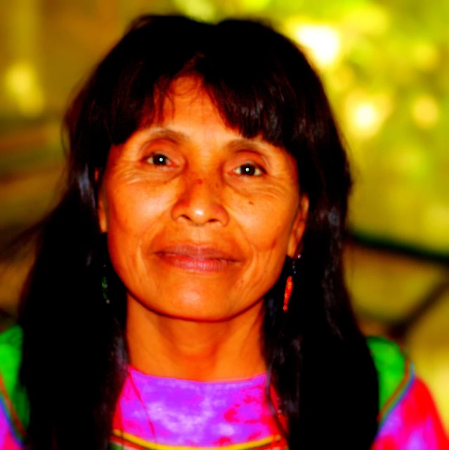 an older woman with long black hair and earrings smiles for the camera