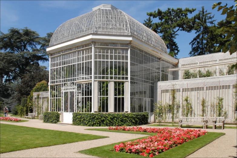 a large glass house with a flower garden behind it