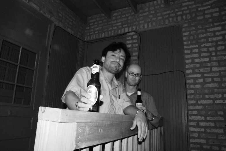 two men sitting on a stair railing, one holding a beer