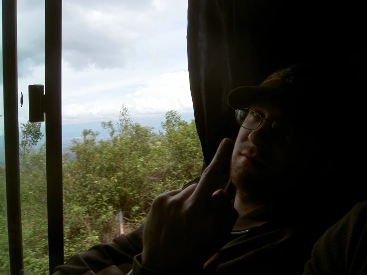 a man sitting next to a window holding his phone up to his ear