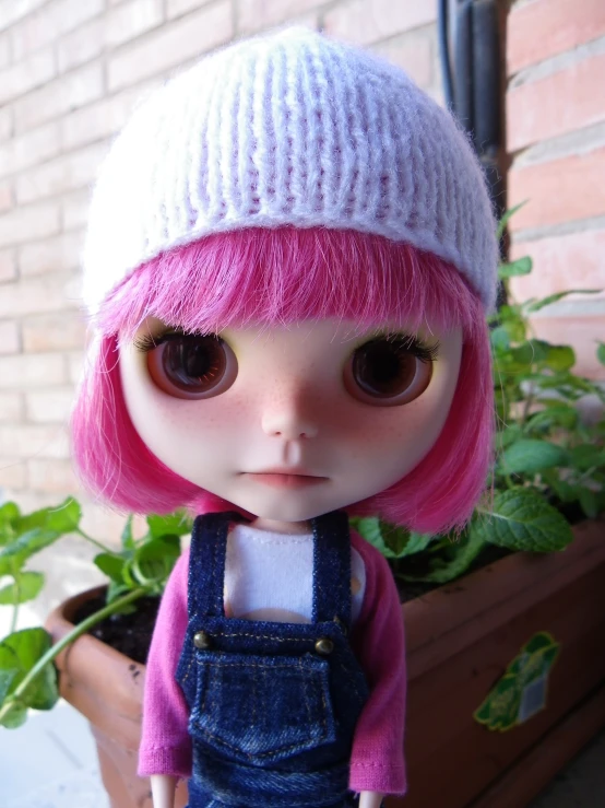 a cute doll with pink hair wearing a blue dungghuist and white hat