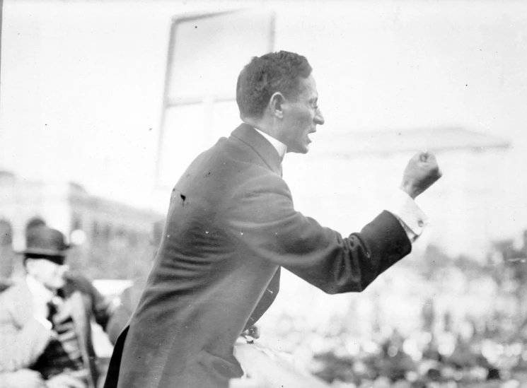 a man in a suit and tie waving at soing in front of an audience