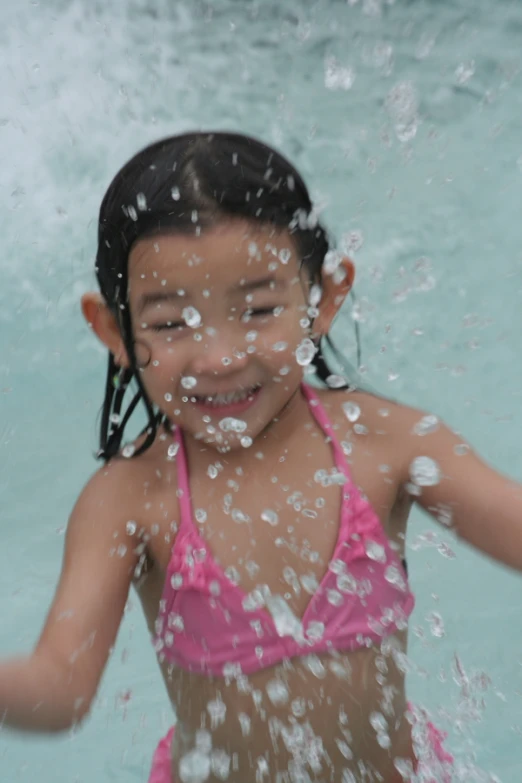 a little girl in pink bathing suit splashing water