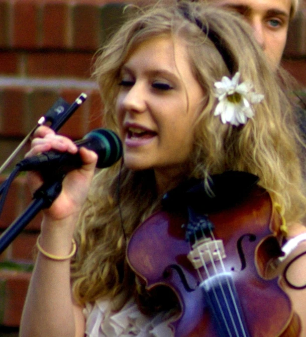 a girl in white shirt playing violin while microphone