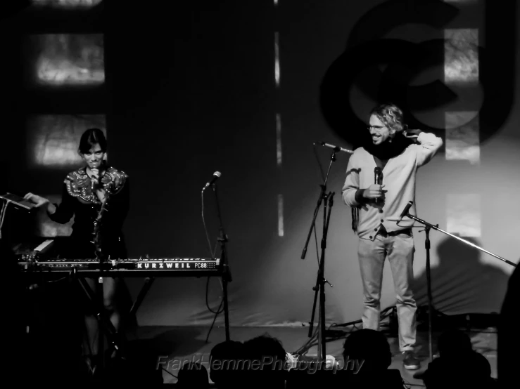 two people on stage one is holding a guitar and the other a keyboard