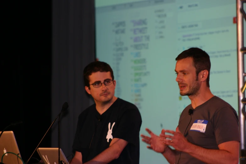 two men talking in front of a projector screen