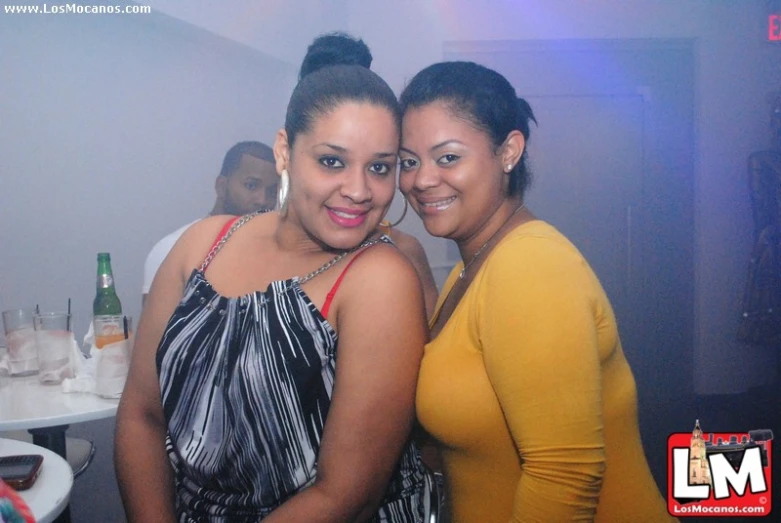 two women pose together in the background as bottles of wine are sitting on the bar