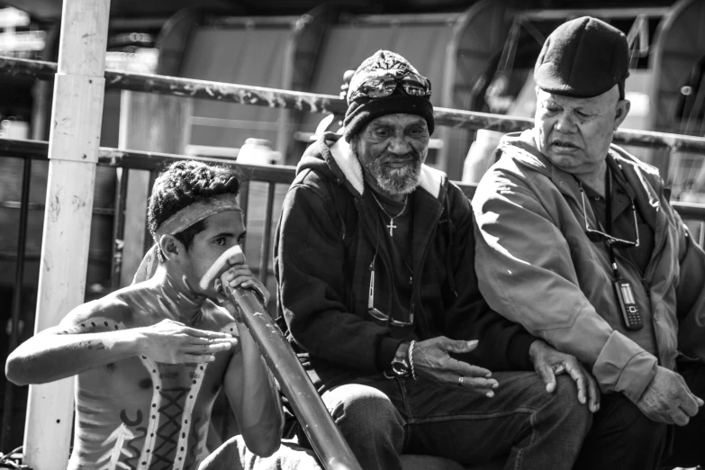 an older man in a black and white po, standing next to two younger men