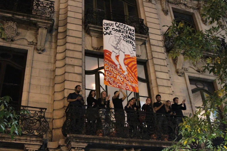 a group of people standing on a balcony next to an orange and white flag