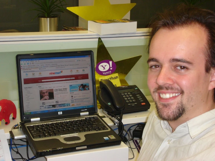 man smiling with phone and laptop on table