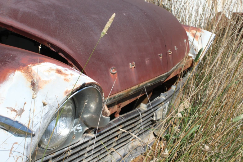 an old rusted out car in a grassy field