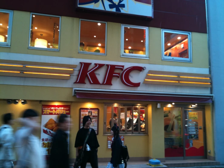 a group of people walking past a kfc restaurant