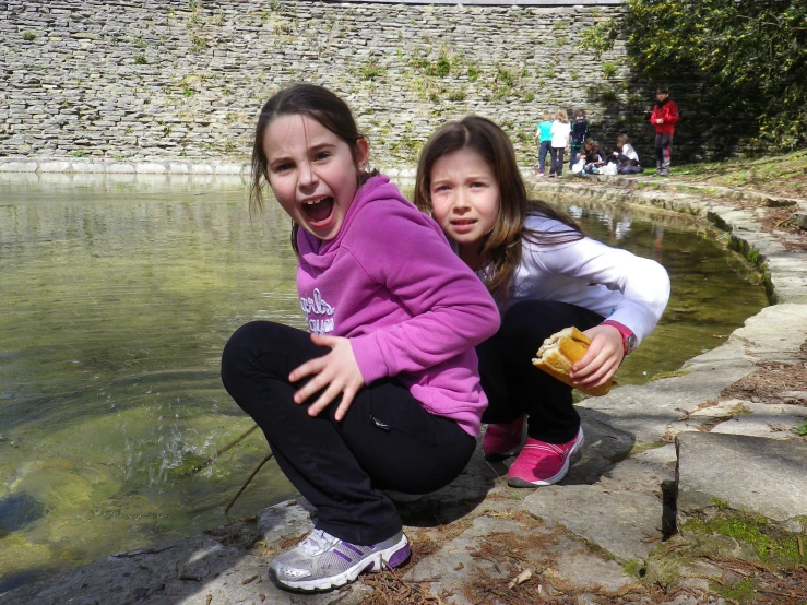two girls crouch near a body of water