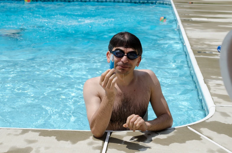 a man in sunglasses sits near a swimming pool