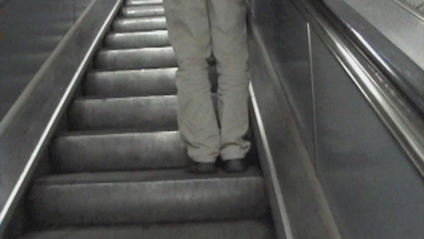 a man riding down the escalator while wearing white pants and an orange jacket