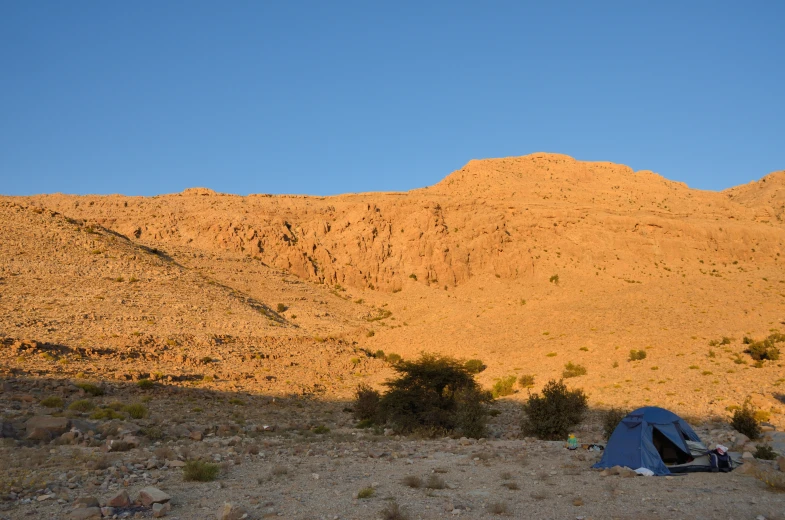 an tents sits on a dirt and grassy area near a mountain
