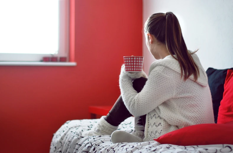 the girl sits on the bed with her cup of coffee