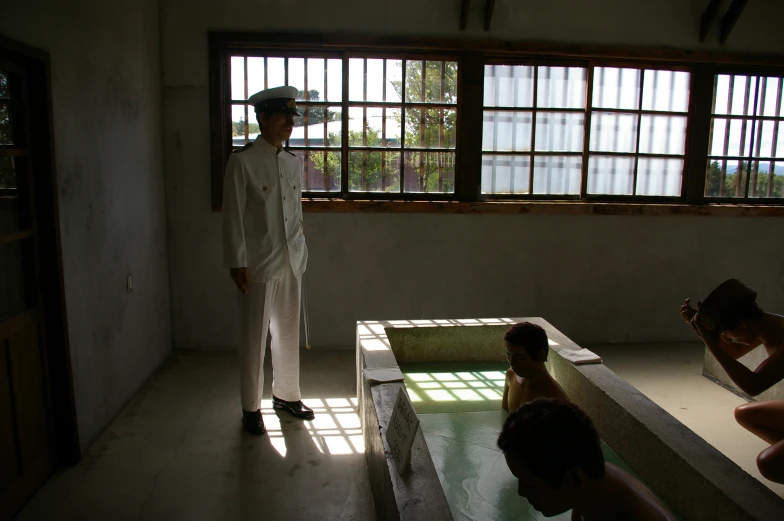 an asian man with a hat, white pants and sunglasses stands next to three people in a pool in a cement building