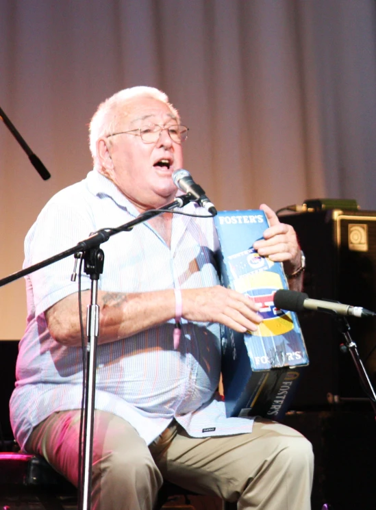 an older man sitting at a microphone and reading a book