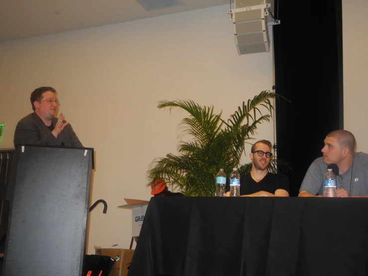 two men on stage talking in front of a black table