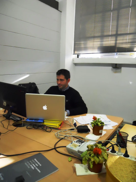 the man sits at a desk working on a laptop