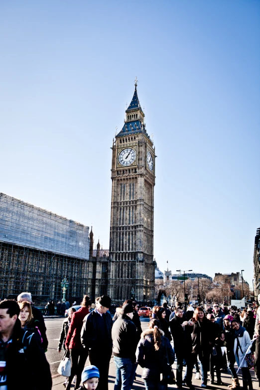 a crowd of people walking down a street past big ben