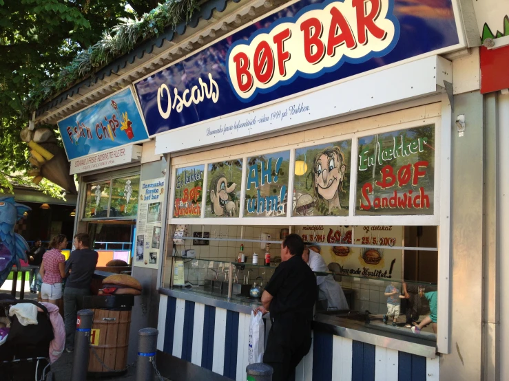 the front of a restaurant with posters and people sitting at tables