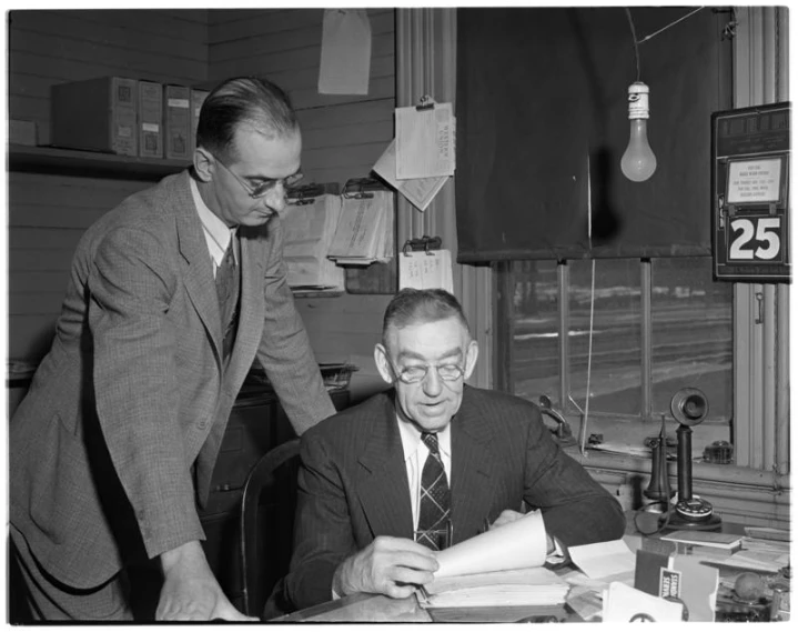 two men work on paperwork at a desk in an office