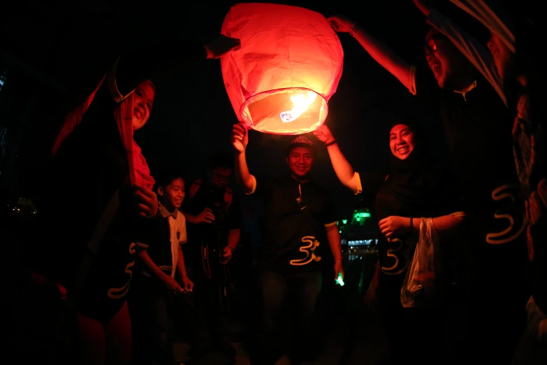 people hold the sky lantern high up in the dark