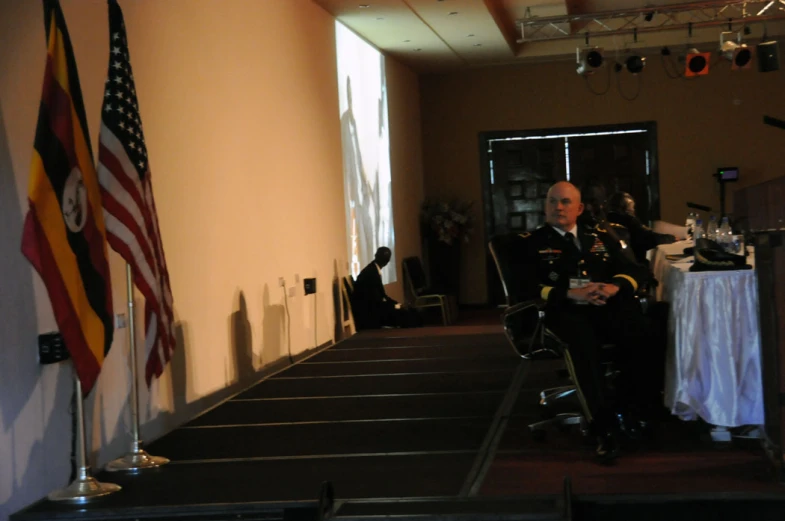 a man sitting at a podium at an event with flags in the background