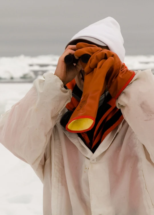 a person in winter clothing with a white hood on and orange gloves and a red scarf on