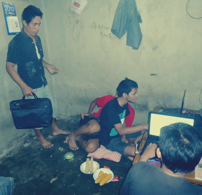 two men sitting on the ground near some other men and a laptop