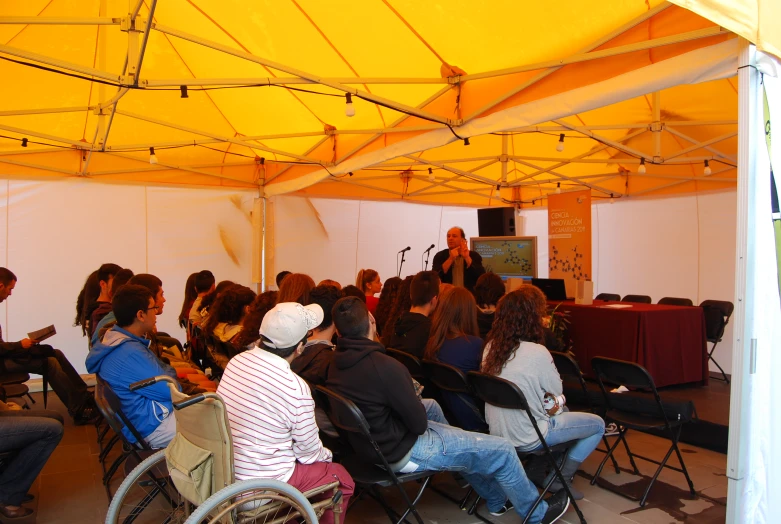 a crowd of people sitting under a yellow tent