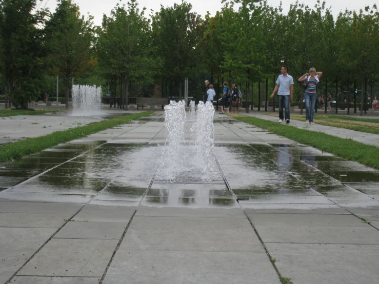 a water fountain in a park with people walking past it